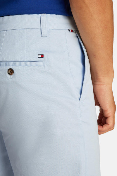 Short bleu clair de Tommy Hilfiger avec poche boutonnée et logo sur l'arrière, porté avec un polo bleu.