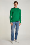 Rechte lichtblauwe spijkerbroek van Tommy Hilfiger, met achterzak versierd met logo, gedragen met een groene trui.