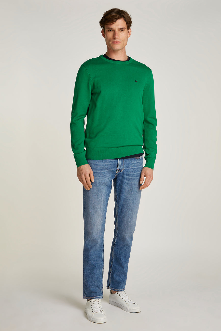 Rechte lichtblauwe spijkerbroek van Tommy Hilfiger, met achterzak versierd met logo, gedragen met een groene trui.