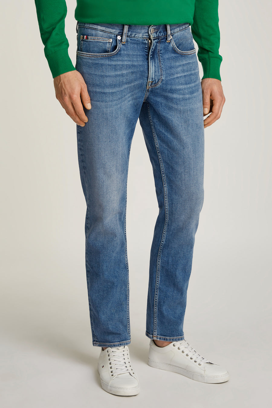Rechte lichtblauwe denim jeans van TOMMY HILFIGER, gedragen met een groene trui en witte sneakers.