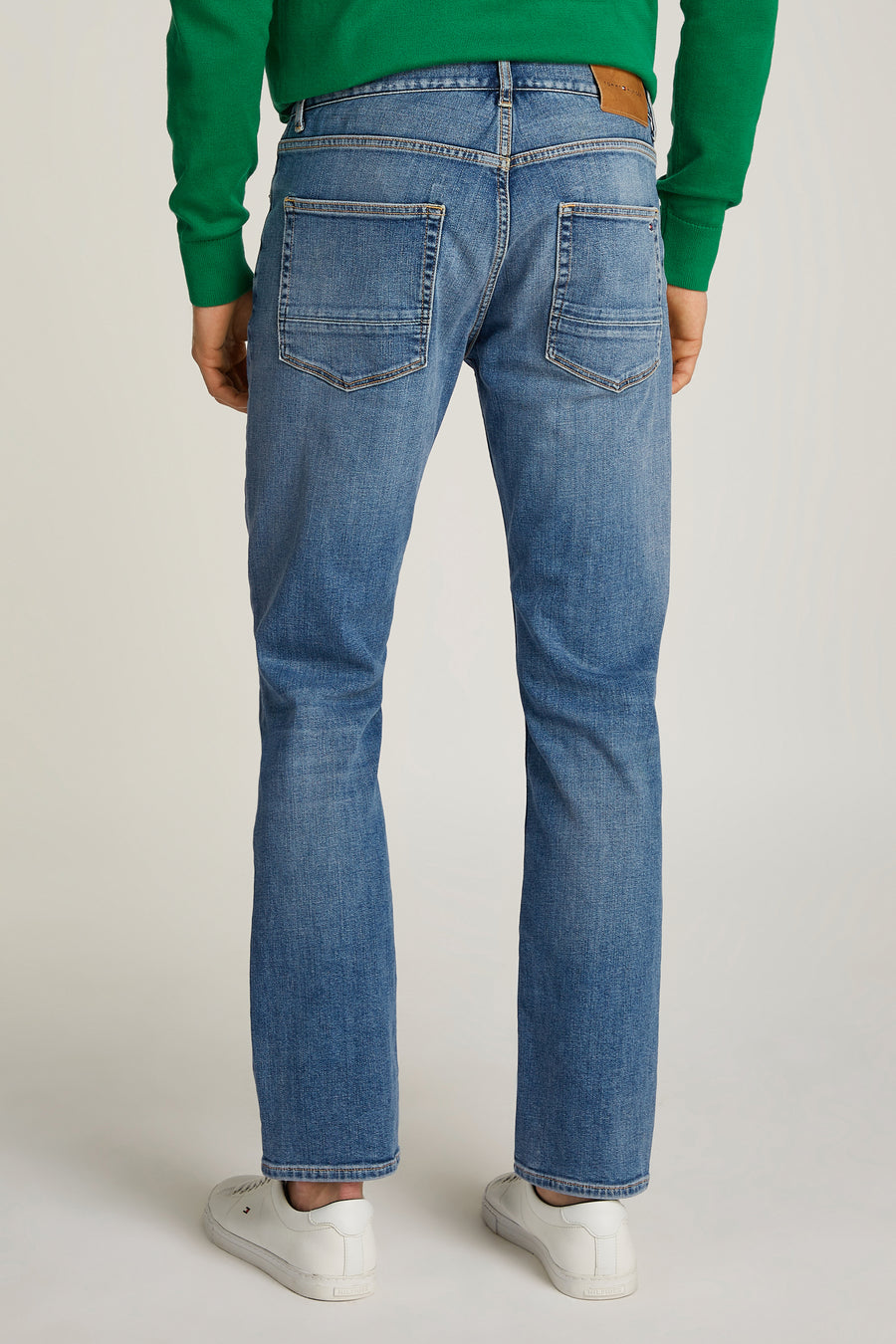 Rechte lichtblauwe spijkerbroek van Tommy Hilfiger met gestructureerde achterzakken, gedragen met een groene trui.