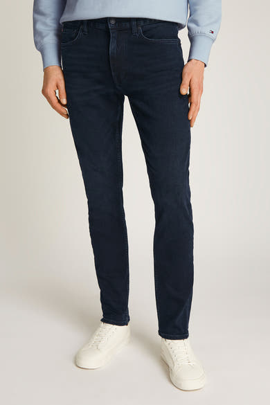 Rechte jeans in zwartblauw denim van TOMMY HILFIGER, gedragen met een lichtblauwe trui en witte sneakers.