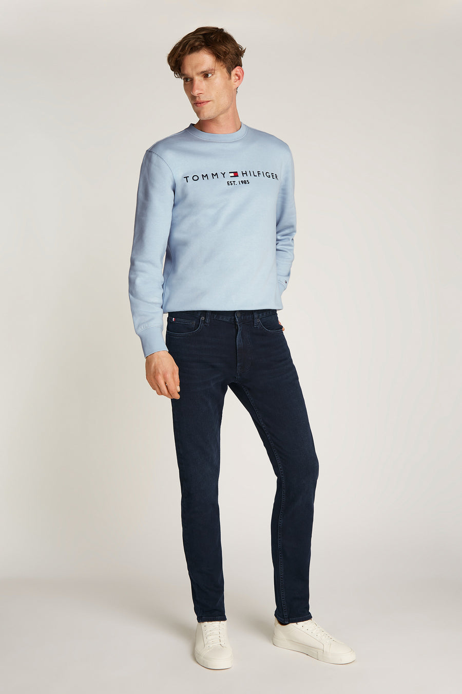 Rechte zwarte denim jeans van Tommy Hilfiger gedragen met een lichtblauwe trui en witte sneakers.