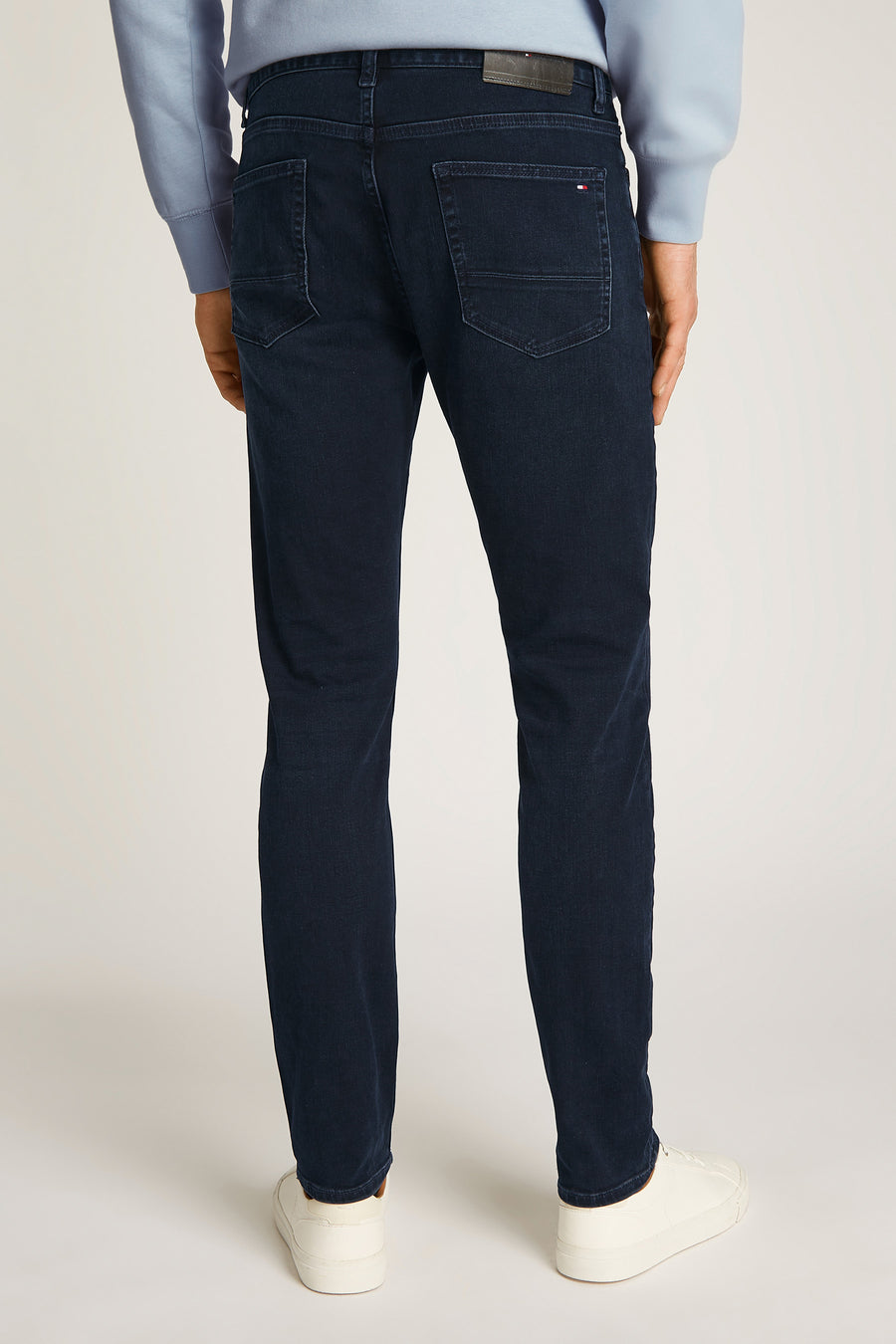 Rechte blauwzwarte spijkerbroek van TOMMY HILFIGER, gedragen met een blauwe trui en witte sneakers.