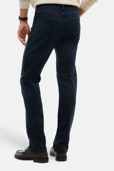 Blue black straight-leg denim jeans by DENTON, back view, featuring clean stitching and classic rear pockets, worn with brown loafers and cream sweater.