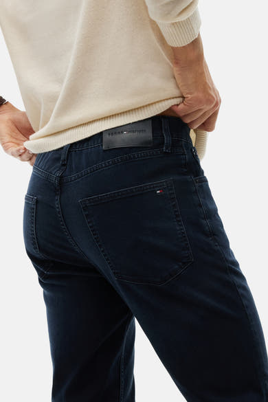 Blue black straight-fit denim jeans by Tommy Hilfiger, back view with branded leather patch and flag tab on pocket, worn with cream ribbed sweater.