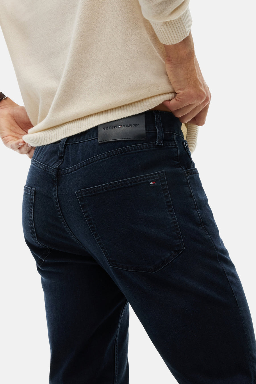 Blue black straight-fit denim jeans by Tommy Hilfiger, back view with branded leather patch and flag tab on pocket, worn with cream ribbed sweater.
