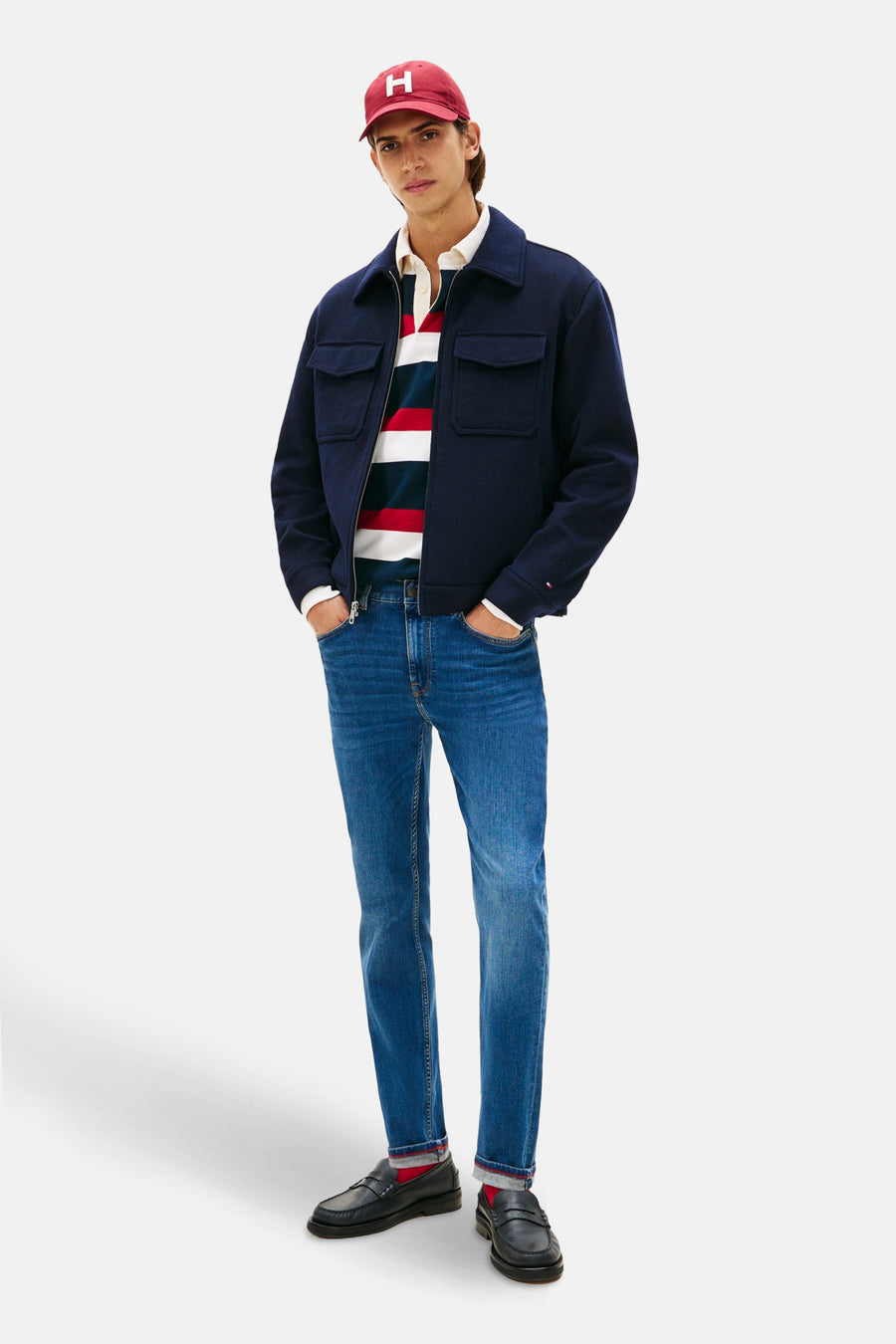 Middelblauwe slim fit jeans van TOMMY HILFIGER, gedragen met een marineblauw jack, een gestreept poloshirt en loafers.