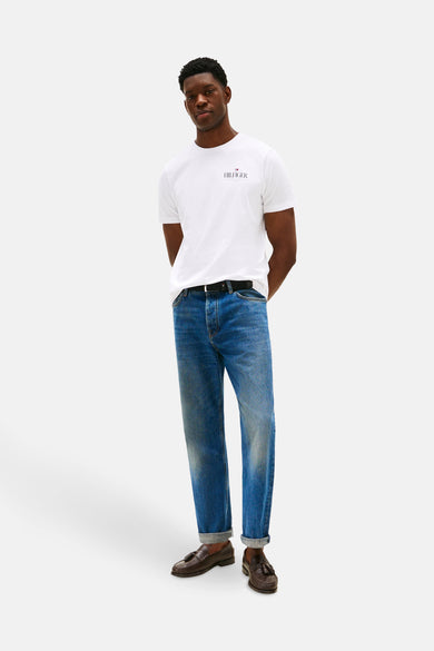 T-shirt à manches courtes blanc de TOMMY HILFIGER, porté avec un jean bleu, ceinture noire et mocassins marron.
