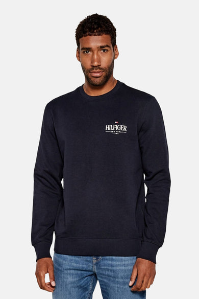 Sweat-shirt bleu marine de Tommy Hilfiger avec logo sur la poitrine et porté avec un jean.
