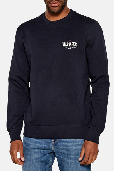 Sweat bleu de TOMMY HILFIGER avec logo sur la poitrine, porté avec un jean décontracté.
