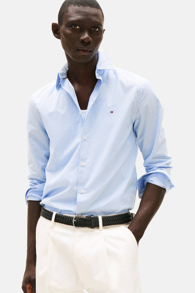 Chemise à manches longues bleue à motifs, de Tommy Hilfiger, portée ouverte sur un débardeur blanc, avec une ceinture noire.
