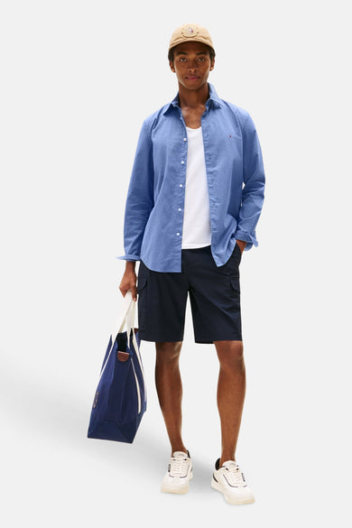 Chemise à manches longues bleue à pois par TOMMY HILFIGER, portée sur un t-shirt blanc, avec un short cargo bleu marine et un chapeau beige.