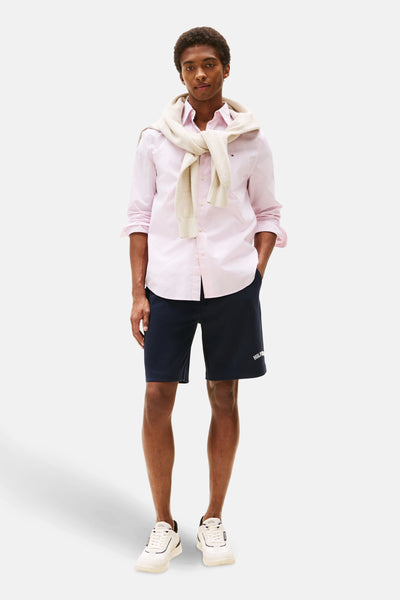 Roze overhemd met lange mouwen en stippen, van TOMMY HILFIGER, gedragen met een beige trui geknoopt over de schouders en een marineblauwe korte broek.