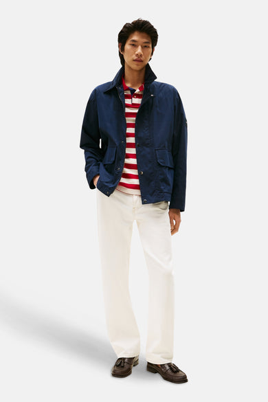 Veste bleue de TOMMY HILFIGER, portée sur un polo rayé rouge et blanc, avec un pantalon blanc et des mocassins en cuir marron.