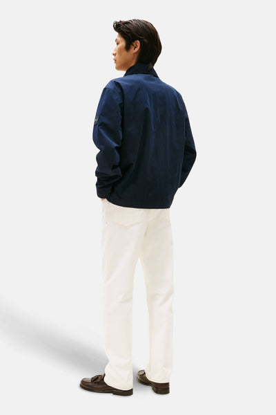 Veste bleu marine de TOMMY HILFIGER, portée avec un pantalon blanc et des chaussures marron