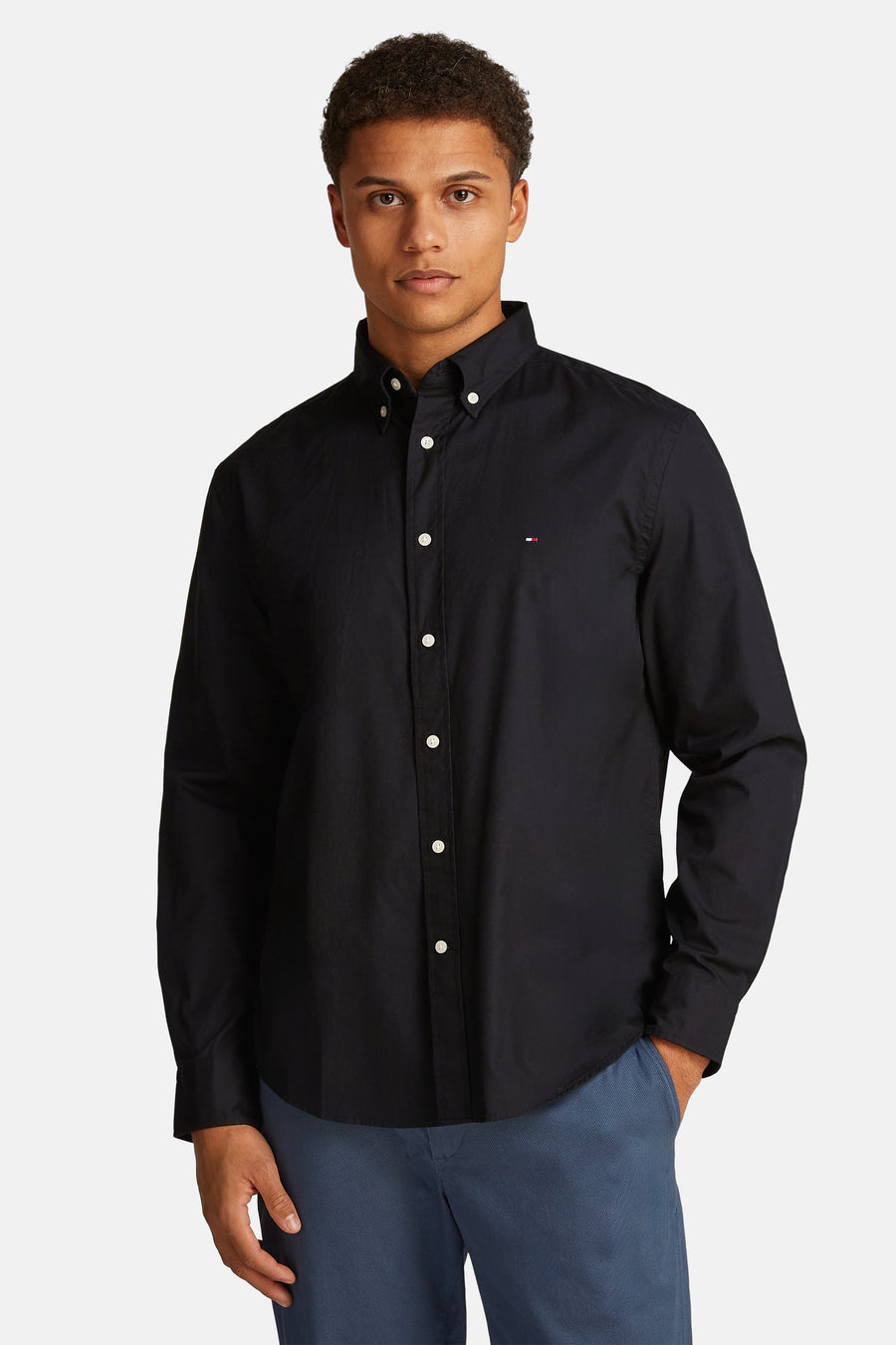 Chemise noire à manches longues de Tommy Hilfiger avec patte de boutonnage blanche, portée avec un pantalon bleu.