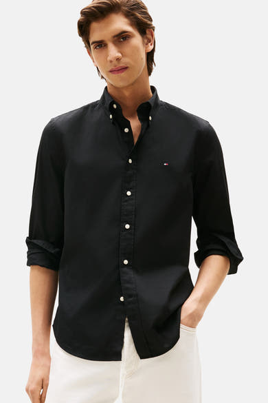 Chemise à manches longues noire de Tommy Hilfiger, boutonnée avec logo subtil sur la poitrine, portée avec un pantalon clair.
