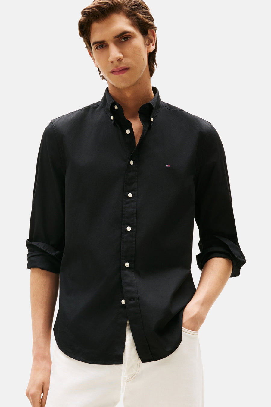 Chemise à manches longues noire de Tommy Hilfiger, boutonnée avec logo subtil sur la poitrine, portée avec un pantalon clair.