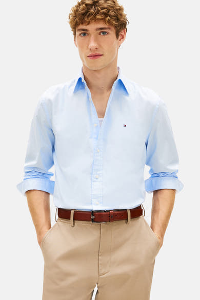 Chemise bleue à manches longues de Tommy Hilfiger avec un pantalon chino beige et une ceinture marron.