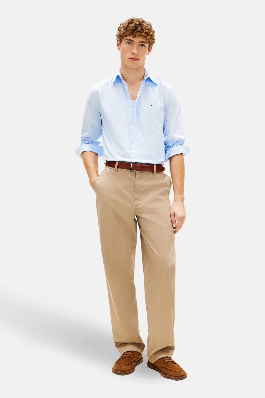 Chemise bleue à manches longues de Tommy Hilfiger, portée ouverte avec un pantalon chino beige et des chaussures marron.