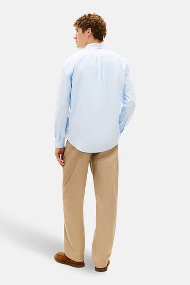 Chemise à manches longues bleue de TOMMY HILFIGER, portée avec un pantalon beige et des mocassins marron, vue de dos.