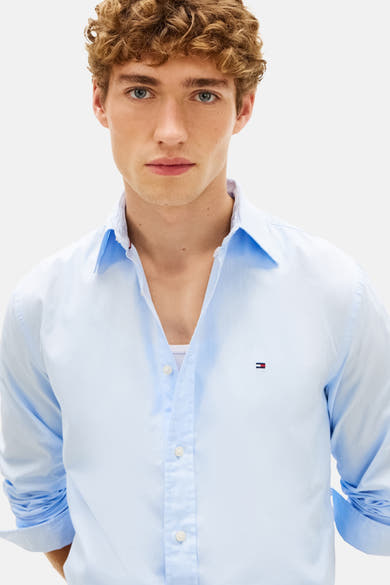 Chemise à manches longues bleue de TOMMY HILFIGER, portée avec un débardeur blanc, boutons apparents.