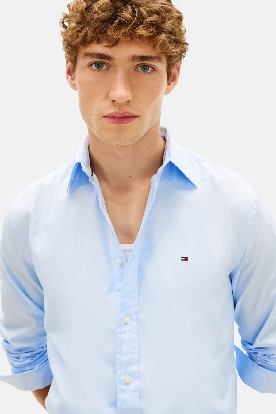 Chemise à manches longues bleue de TOMMY HILFIGER, portée avec un débardeur blanc, boutons apparents.