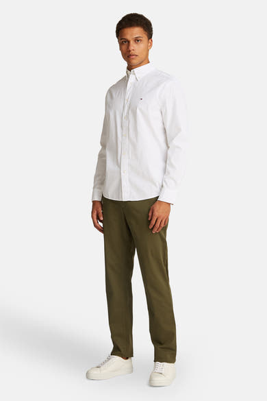 Chemise blanche à manches longues de Tommy Hilfiger, avec une coupe classique, portée avec un pantalon olive et des baskets blanches.