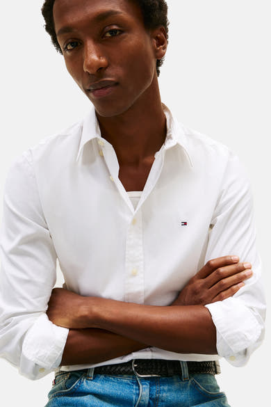 Chemise à manches longues blanche de Tommy Hilfiger, portée ouverte sur un débardeur, avec un jean et une ceinture.