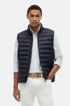 Matblauwe gewatteerde bodywarmer van TOMMY HILFIGER, met klein vlaglogo en gedragen over een gestreept overhemd.