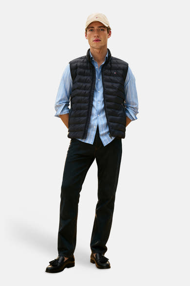 Veste sans manches matelassée noire de TOMMY HILFIGER sur chemise rayée bleue, jean foncé et mocassins.