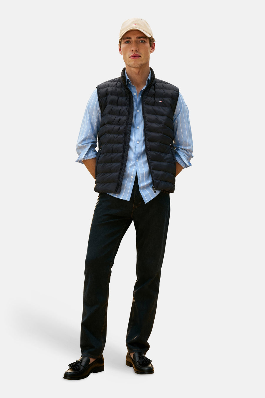 Veste sans manches matelassée noire de TOMMY HILFIGER sur chemise rayée bleue, jean foncé et mocassins.