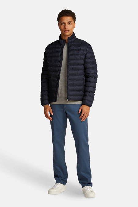 Veste courte bleue matelassée de TOMMY HILFIGER avec col montant, portée sur un pull gris, un pantalon bleu et des baskets blanches.
