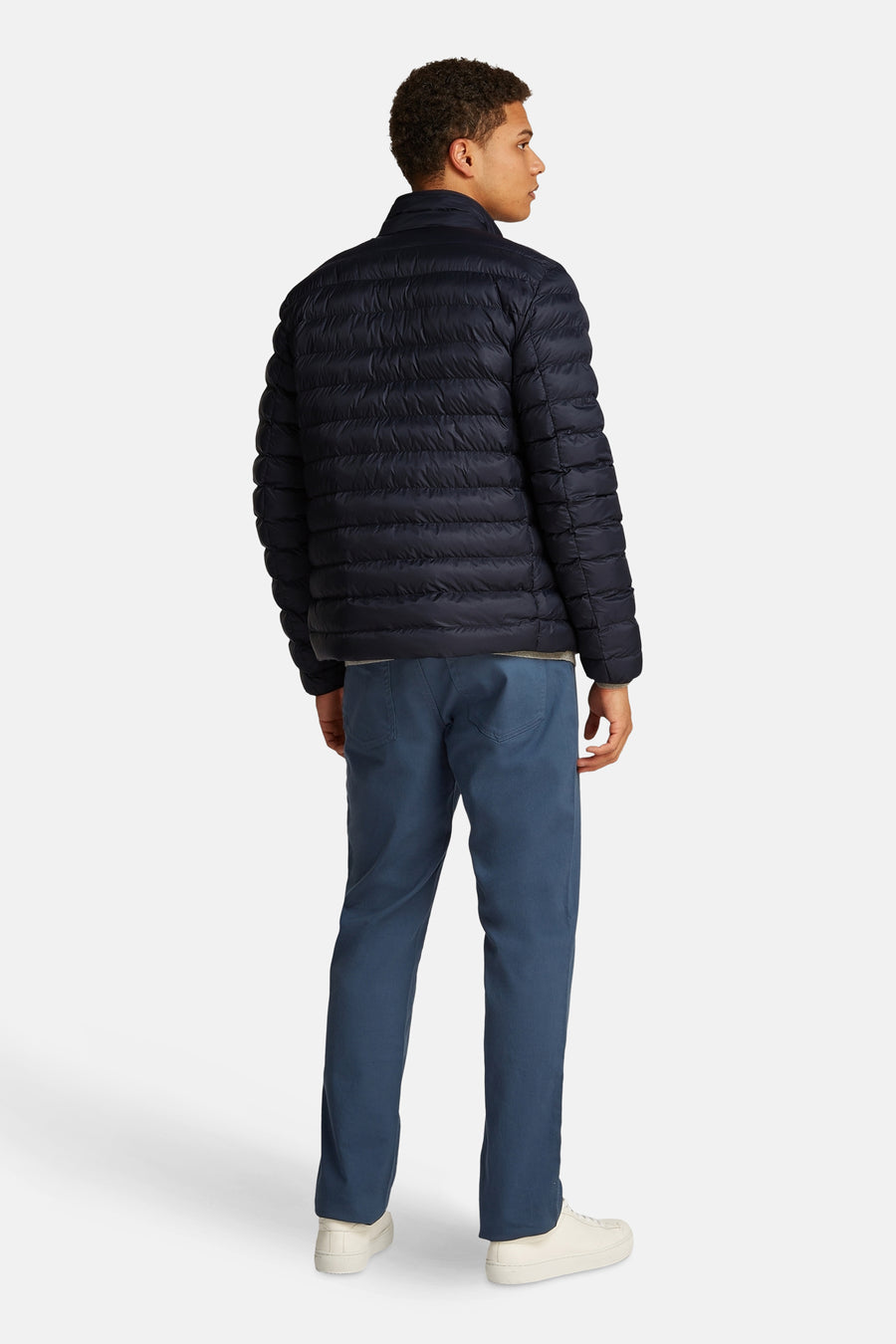 Veste courte bleue de TOMMY HILFIGER matelassée, vue de dos sur un homme avec un pantalon bleu et des baskets.