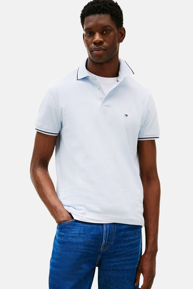 Polo à manches courtes bleu de TOMMY HILFIGER, porté avec un jean bleu, une bordure marine au col et aux manches.