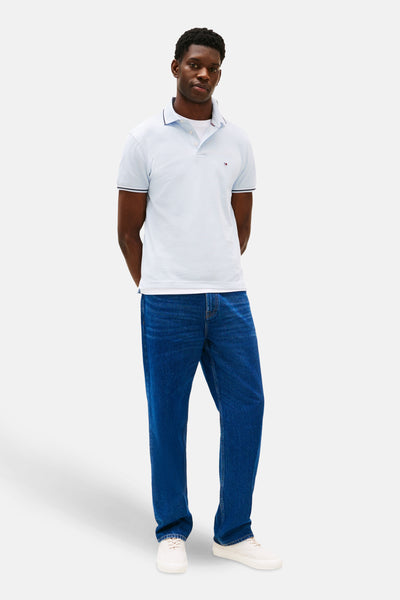 Polo à manches courtes bleu de TOMMY HILFIGER, porté avec un jean bleu et des baskets blanches.