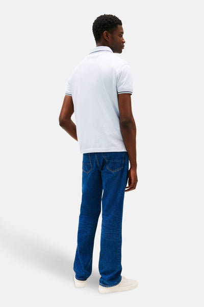 Polo bleu à manches courtes de TOMMY HILFIGER, porté avec un jean bleu et des baskets couleur crème, vue de dos.
