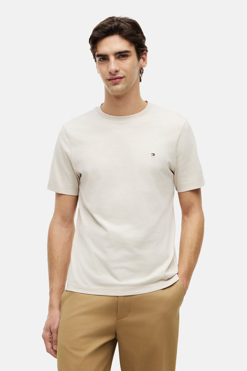 T-shirt écru de Tommy Hilfiger, uni avec le logo de la marque sur la poitrine, porté avec un pantalon marron.