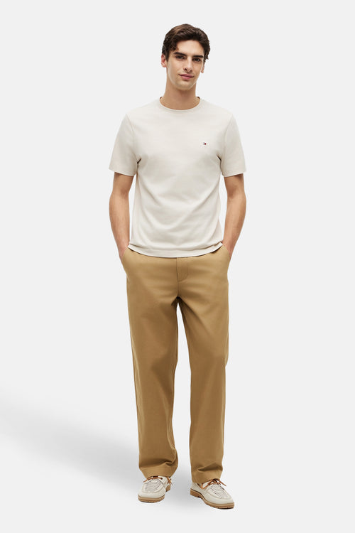 T-shirt écru de TOMMY HILFIGER, porté avec un pantalon marron et des chaussures bateau beiges à lacets.