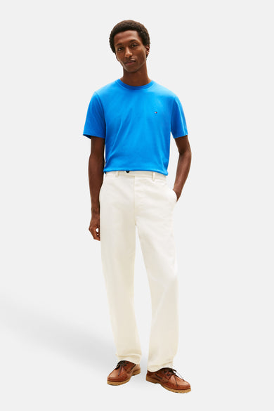 T-shirt bleu à manches courtes par TOMMY HILFIGER, porté avec un pantalon blanc et des chaussures bateau marron.