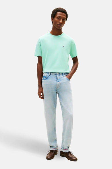 T-shirt bleu clair de TOMMY HILFIGER, avec logo discret, porté avec un jean délavé et des chaussures marron.