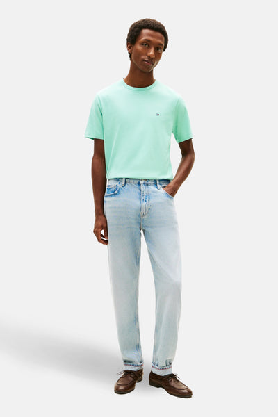 T-shirt bleu clair de TOMMY HILFIGER, avec logo discret, porté avec un jean délavé et des chaussures marron.
