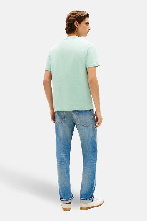 T-shirt vert à manches courtes de TOMMY HILFIGER, porté avec un jean bleu et des baskets blanches.