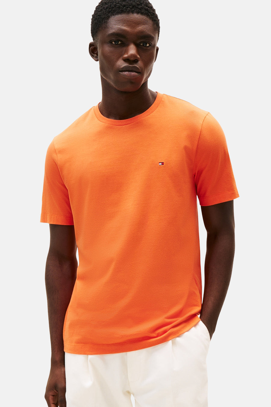 T-shirt orange à manches courtes de TOMMY HILFIGER, porté avec un pantalon blanc décontracté.