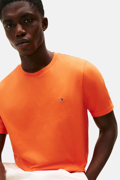 T-shirt orange à manches courtes de TOMMY HILFIGER, porté par un homme au teint foncé.