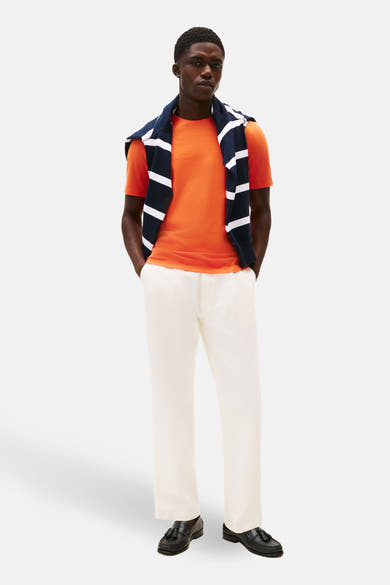 T-shirt orange à manches courtes de TOMMY HILFIGER avec un pull rayé marine et un pantalon blanc.