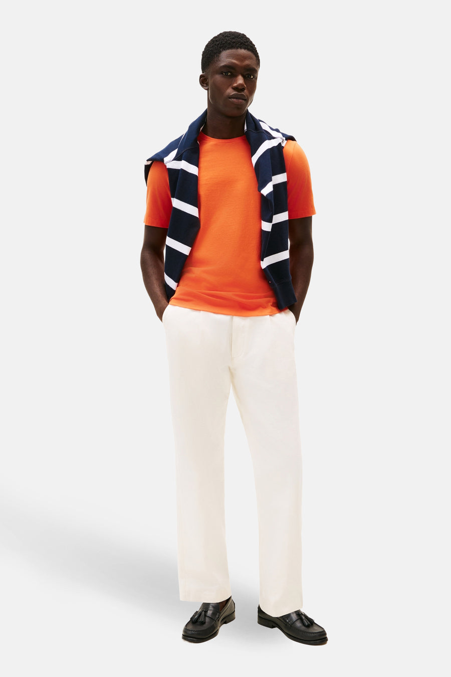T-shirt orange à manches courtes de TOMMY HILFIGER avec un pull rayé marine et un pantalon blanc.