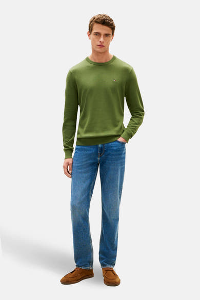 Pull à col rond vert de TOMMY HILFIGER, porté avec un jean bleu et des chaussures marron en daim.