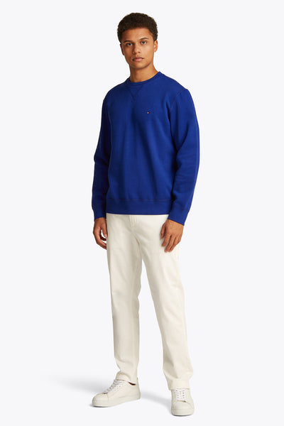 Blauwe rondehals sweatshirt van TOMMY HILFIGER gedragen met gebroken witte broek en witte sneakers.